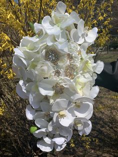 a bridal bouquet with white flowers in the foreground and yellow trees in the background