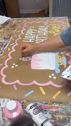 a woman is painting a birthday cake on a cardboard board with icing and sprinkles