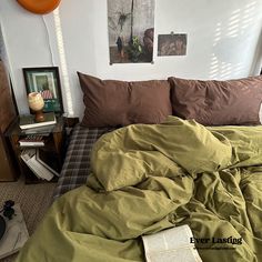 an unmade bed with green sheets and brown pillow cases in a small bedroom area