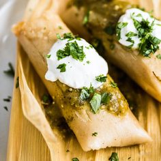 two burritos topped with sour cream and cilantro on a wooden plate