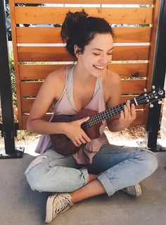 a woman sitting on the ground playing a ukulele with her eyes closed and smiling