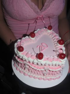 a woman holding a heart shaped cake with cherries on the top and pink icing