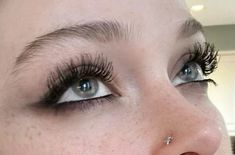 a close up of a woman's face with long lashes and piercings on her nose