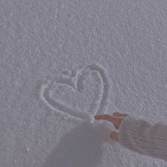 a person is standing in the snow with their hand out towards a heart drawn in the snow