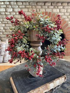 a vase filled with red berries and greenery on top of a table next to an old book