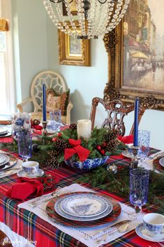 a dining room table set for christmas with plates and silverware, candlesticks and pine cones