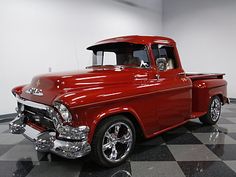 an old red truck is parked on a black and white checkered floor