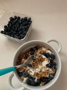 a bowl of granola with blueberries and yogurt next to a container of strawberries