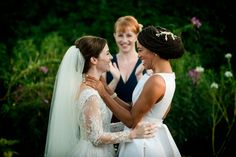 two brides laugh as they stand next to each other in front of some flowers