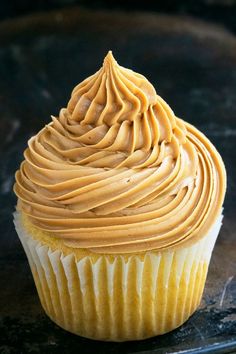 a cupcake with frosting sitting on top of a metal tray in front of a black surface