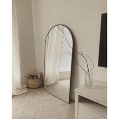 a mirror sitting on top of a white dresser next to a vase filled with flowers