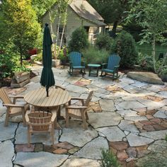 a patio with chairs and an umbrella in the middle is surrounded by stone pavers