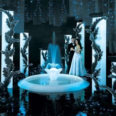 a man and woman standing in front of a fountain with blue lights on the water