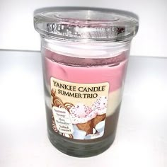 a pink candle is sitting on a white counter top next to a glass jar with an image of a cupcake in it