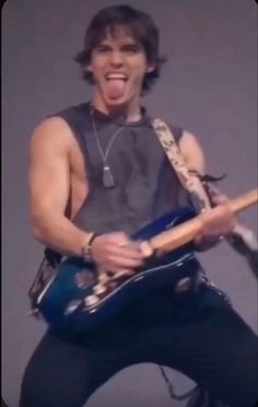 a man holding a blue guitar in his right hand and making a funny face with his mouth wide open