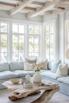 a living room filled with white furniture and lots of window sill space next to a large wooden coffee table