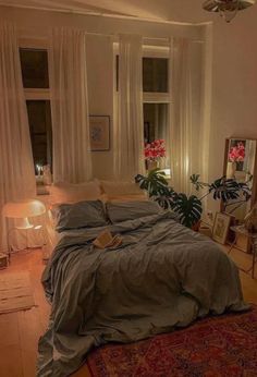 a bed sitting in a bedroom next to a window filled with curtains and pillows on top of a wooden floor