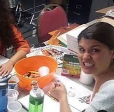 two women sitting at a table with drinks and papers in front of them, smiling