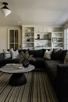 a living room filled with black furniture and lots of pillows on top of the couch