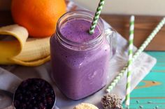 a purple smoothie in a mason jar with two straws next to it and some fruit