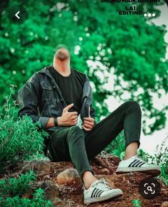 a man sitting on top of a tree stump next to green trees and bushes with his hands in his pockets