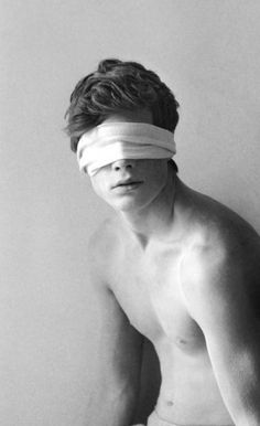 a shirtless man with blind folded over his eyes and head is leaning against a wall