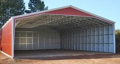 a red and white metal building sitting in the middle of a dirt field next to trees