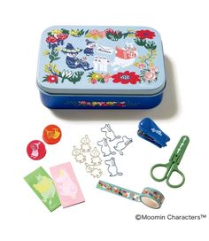 a tin with scissors and some stickers next to it on a white table top