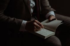 a man in a suit writing on a notepad with a pen and paper next to him