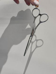 a pair of scissors being held up by someone's hand on a white surface