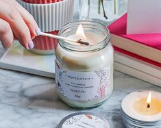 a person lighting a candle in a glass jar on a table next to other candles