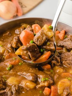 a ladle full of beef stew with carrots and potatoes is being held by a spoon