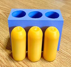 three yellow candles sitting in front of a blue box on a wooden table with four smaller ones