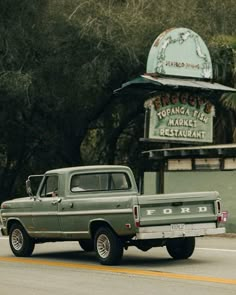 an old pick up truck is driving down the street in front of a business sign