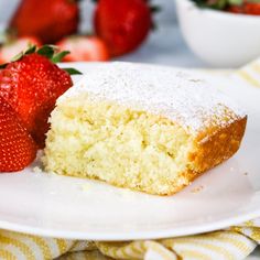 a piece of cake with powdered sugar on top and strawberries in the background