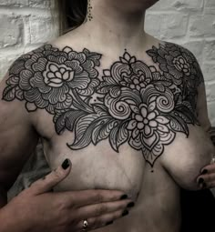 a woman's chest with an intricate tattoo design on her left shoulder and chest