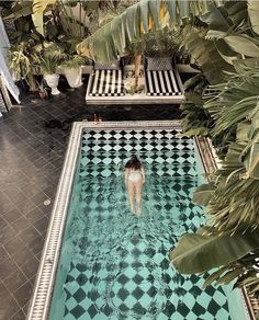 a woman is swimming in a pool surrounded by palm trees and other tropical foliages