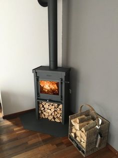 a wood burning stove next to a stack of firewood in a room with hard wood flooring