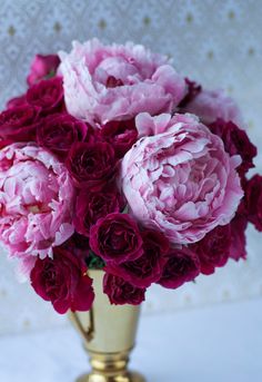 a gold vase filled with pink flowers on top of a white tableclothed wall