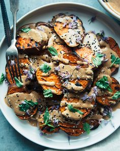 a white plate topped with grilled sweet potatoes covered in gravy and garnished with herbs