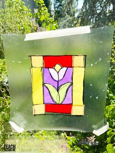 a piece of stained glass with a flower on it in front of some green bushes