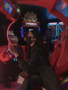 a woman wearing a face mask sitting in front of a video game machine at night