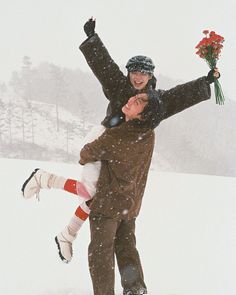 a man and woman are standing in the snow with their arms around each other as they hold flowers