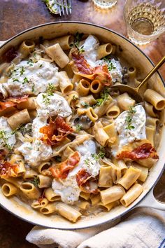 a bowl filled with pasta and sauce on top of a wooden table next to utensils