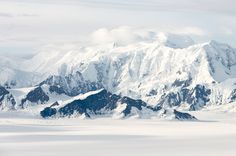 the mountains are covered in snow and have very large peaks on them, as well as clouds