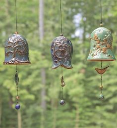 three bells hanging from strings in front of a window with trees behind them and one bell on the other side