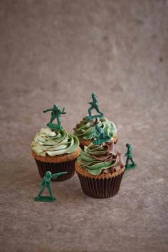 two cupcakes with green frosting and toy soldiers on top are sitting next to each other