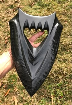 a hand holding a black plastic object in the shape of a heart on top of grass