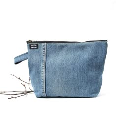 a small denim pouch with zippers on the front and side, sitting next to a twig