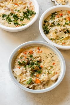 three bowls filled with different types of food on top of a white countertop next to silver spoons